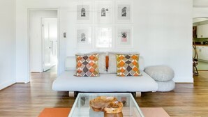 A modern living room with a sofa, patterned cushions, a glass coffee table, and framed pictures on the wall.