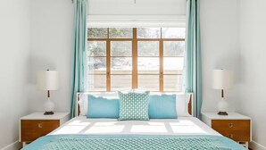 A bedroom with a large bed, two bedside tables, a window with curtains, and a view of the outside.