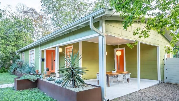 A modern house with a covered patio, a dining area, and a well-maintained garden.