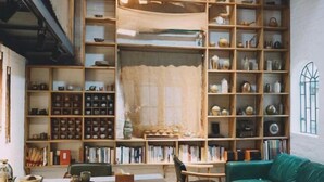 Una habitación acogedora con un sofá verde, una estantería de madera llena de libros y objetos decorativos, y una mesa con algunos objetos encima.