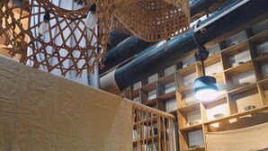 Una habitación con estética rústica, que presenta vigas de madera expuestas, una cesta trenzada colgando del techo y estantes llenos de libros y objetos decorativos.