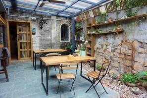 A rustic patio with a wooden table and chairs, stone walls, and a variety of potted plants. - Chunshanwai Guesthouse (Zhuhai)