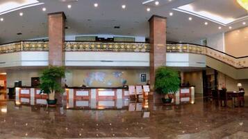 A spacious lobby with a reception desk, two large pillars, and a balcony with a railing.