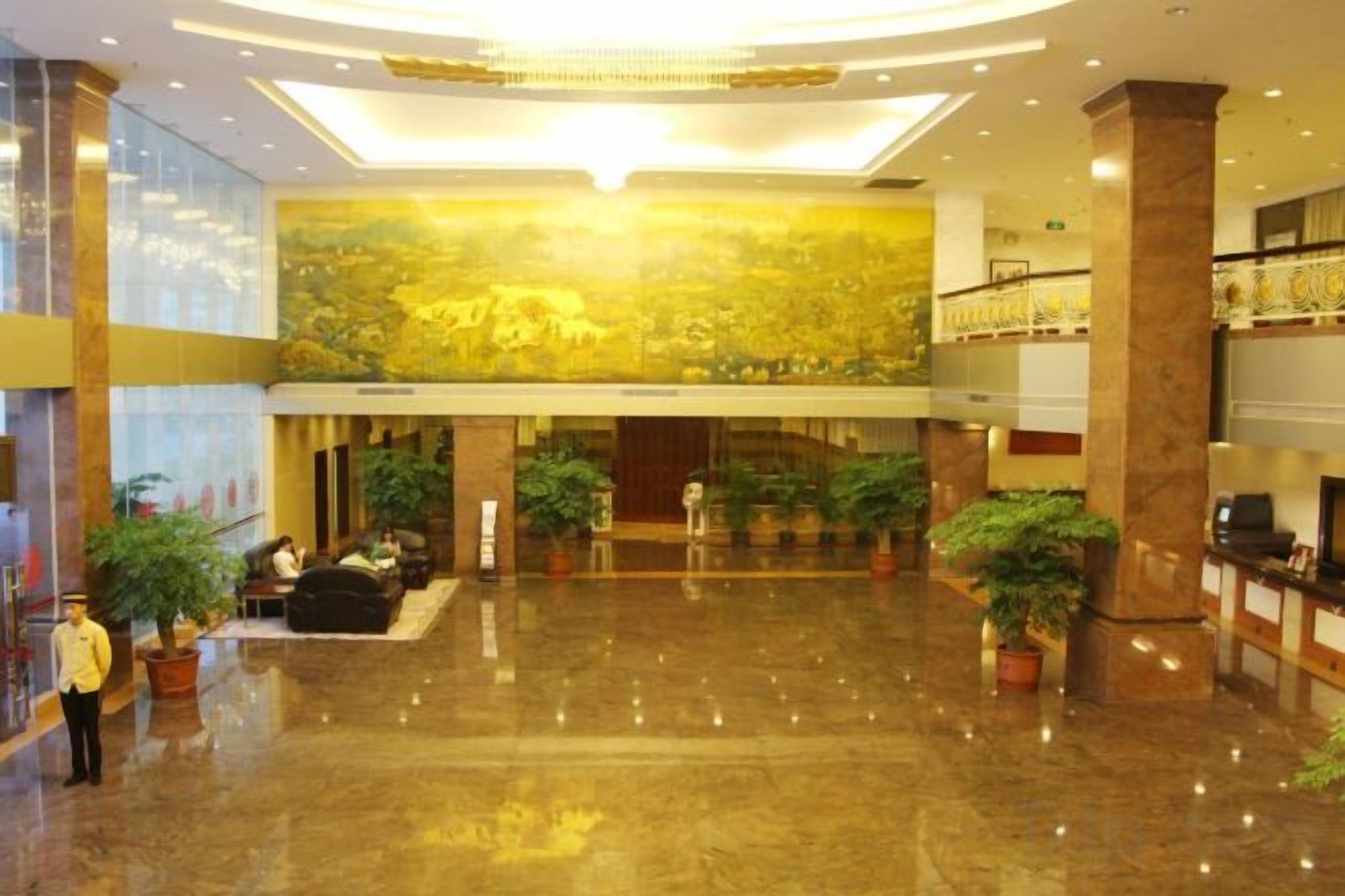 A spacious lobby with a high ceiling, polished floors, and several potted plants.