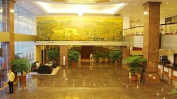 A spacious lobby with a high ceiling, polished floors, and several potted plants.