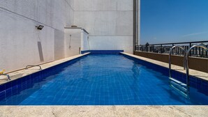 Ein Swimmingpool mit blauen Fliesen, Metallgeländern und einer Betonmauer.