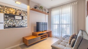 Ein modernes Wohnzimmer mit Flachbildfernseher, Einbauschränken, einer Couch und einem großen Fenster mit leichtem Vorhang.