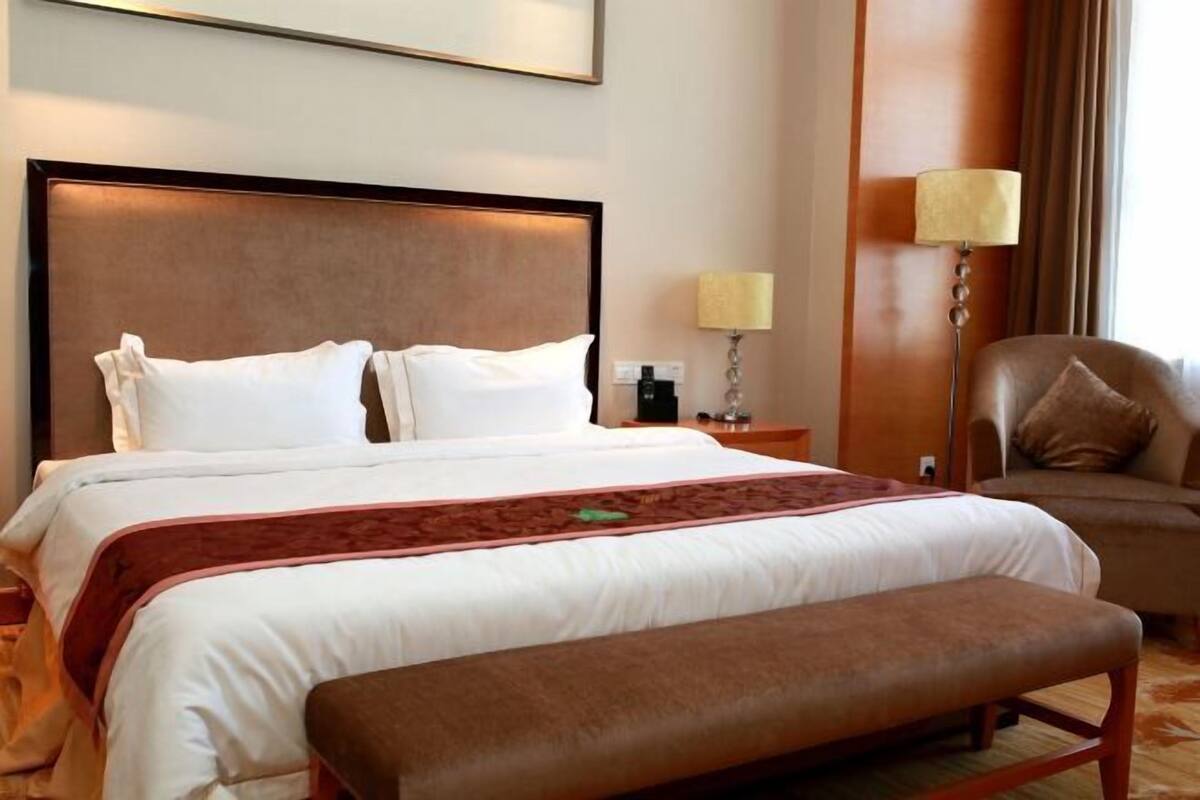 Habitación de hotel con una cama grande, un banco, una lámpara y una silla.