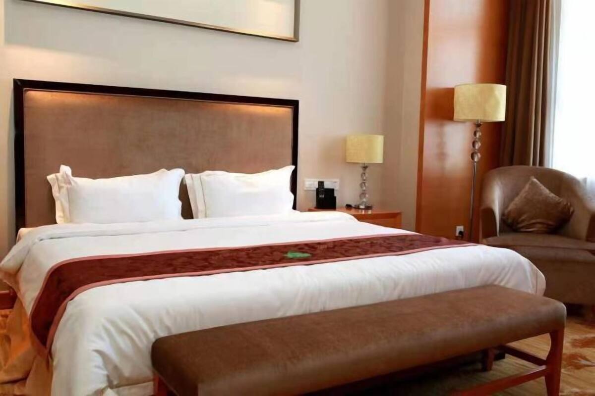 Una habitación de hotel con una cama grande, una mesita de noche, una lámpara y una silla.