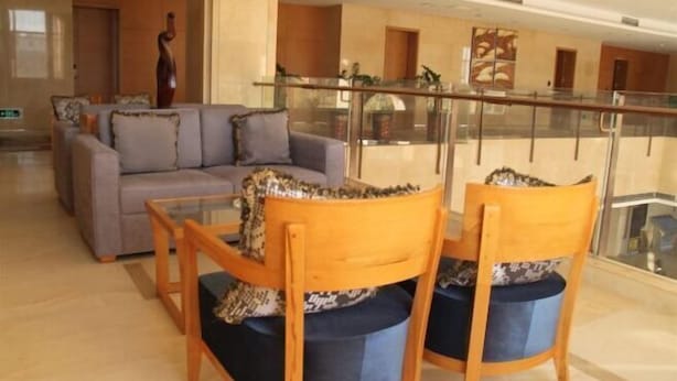 A lobby with a sofa, two wooden chairs, a glass railing, and a decorative sculpture.