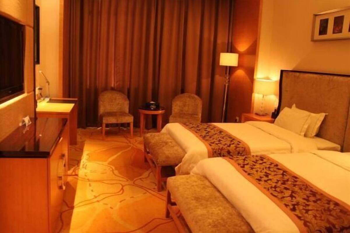 Una habitación de hotel con una cama, dos sillones, un escritorio, una lámpara y un televisor.
