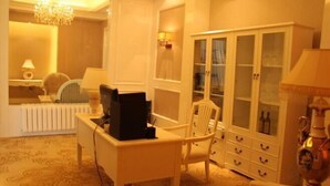 A room with a white desk, a chair, a cabinet with glass doors, a radiator, and a chandelier.