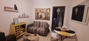 A living room with a sofa, a coffee table, a dining table with chairs, a bookshelf, and a wall with a guitar painting. - Lindo em Copacabana a 1 Quadra da Praia (Rio de Janeiro)