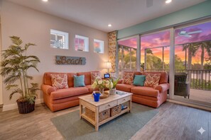A living room with two sofas, a coffee table, a large window with a view, and a wall-mounted sign. - Sunset Seacret by Coastal Chic Vacations (Bradenton)