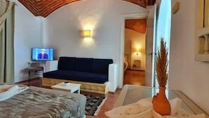 A hotel room with a brick ceiling, a bed, a sofa, a TV, and a large window. - Hôtel Écrin hamammet  (Hammamet)