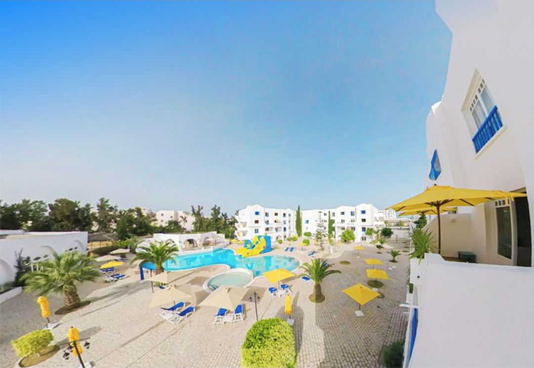Un resort con zona de piscina, tumbonas y un cielo azul despejado.