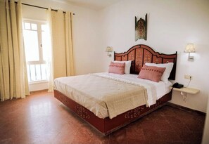 Un dormitorio con una cama grande, dos mesitas de noche con lámparas, una ventana con cortinas y una obra de arte en la pared.