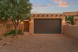 A residential garage with a dark door, a wooden fence, and a gravel driveway. - Restored Casita · Big Views · Walk to Plaza (Santa Fe)