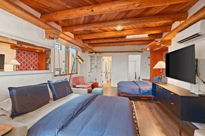 A hotel room with a wooden ceiling, a bed with blue bedding, a desk with a computer, and a TV.
