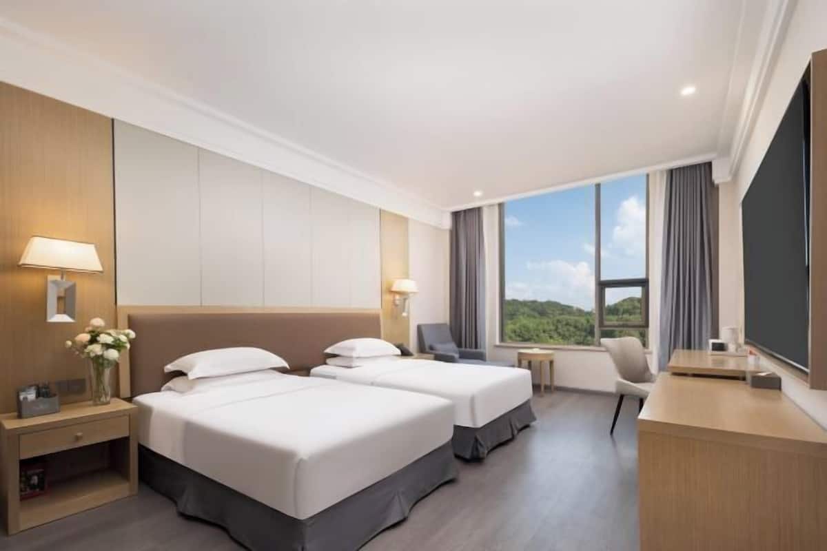A hotel room with two beds, a desk, a chair, a TV, and a window with a view.