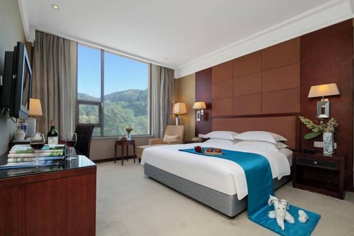 A hotel room with a large bed, a desk with a computer, a chair, a TV, and a view of the outdoors.