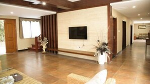 A spacious living area with a flat-screen TV mounted on a wall, a staircase, and a large potted plant.