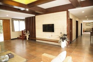 A spacious living area with a flat-screen TV mounted on a wall, a staircase, and a large potted plant. - Xianning Hot Spring Valley Resort (Xianning)