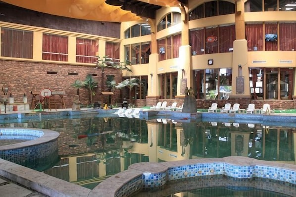 A large indoor pool with clear water, surrounded by lounge chairs and a brick wall.