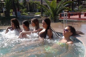 A group of people in a hot tub with a poolside area, palm trees, and a building in the background. - Xianning Hot Spring Valley Resort (Xianning)