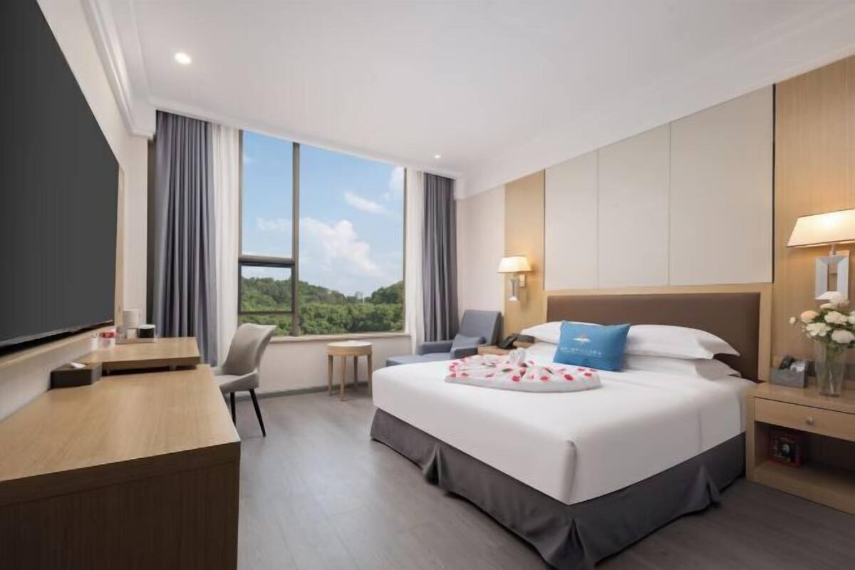 A hotel room with a large bed, a desk, a chair, a small table, and a TV.