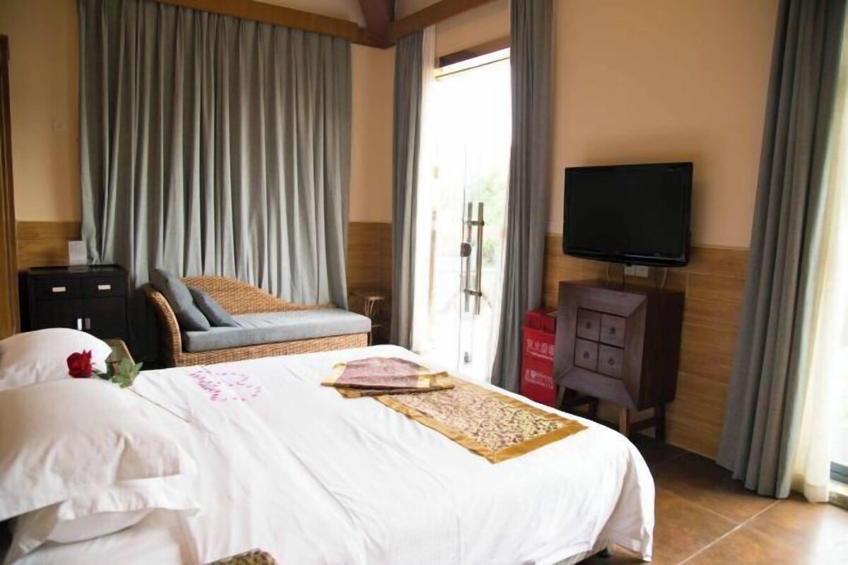 A hotel room with a bed, a television, a wooden cabinet, and a window with curtains.