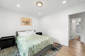 A bedroom with a bed, nightstands, a painting on the wall, and a hallway leading to another room. - Beautiful 2-bedroom near Ocean Beach, Pacific Beach, Sea World, Downtown, & more (San Diego)