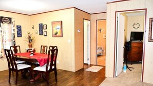 A dining area with a wooden table and chairs, a red tablecloth, and a vase with flowers. There are framed pictures on the wall and a door leading to another room. - Handicap Accessible Private Spacious Beautiful Family Home 5 Acres Pet Friendly  (Homosassa)