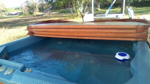 A hot tub with a wooden lid, a blue and white floating device, and a stone-like texture around the edges. - Handicap Accessible Private Spacious Beautiful Family Home 5 Acres Pet Friendly  (Homosassa)