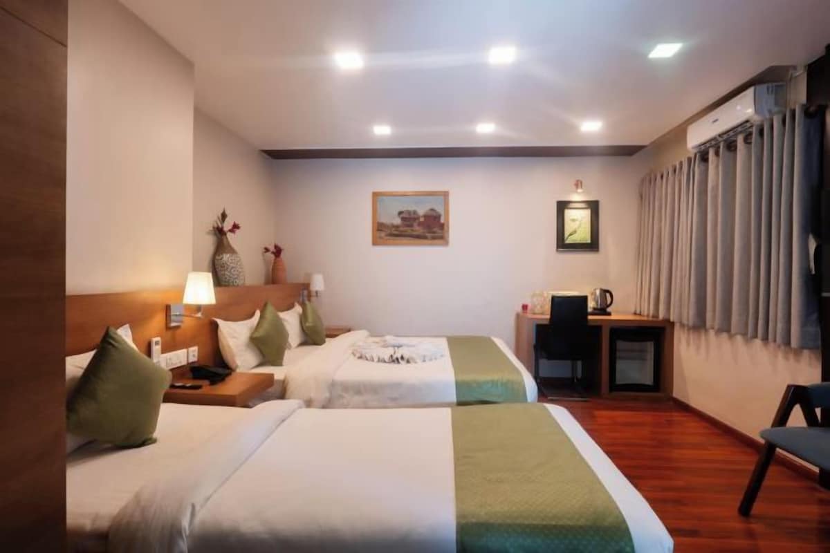 A hotel room with two beds, a desk with a chair, a small table, and a window with curtains.