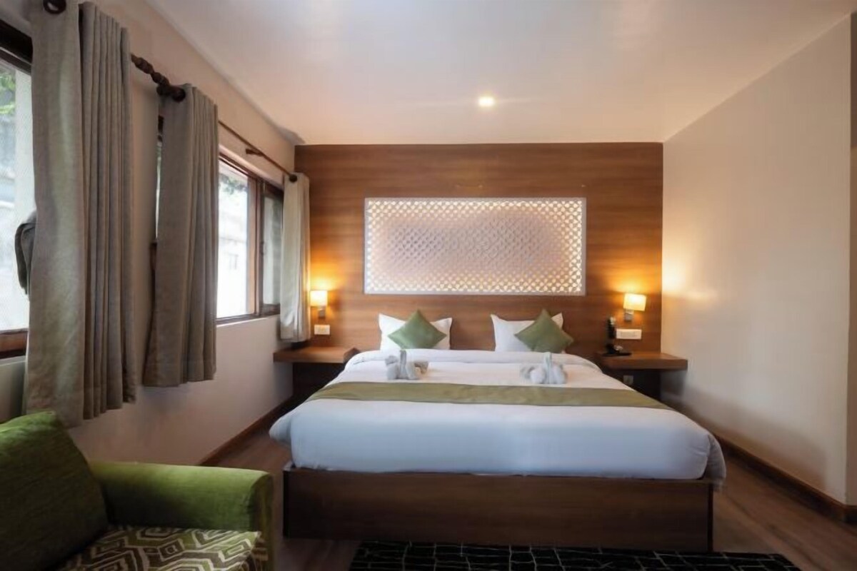 A hotel room with a large bed, two bedside tables, a window with curtains, and a wooden headboard.