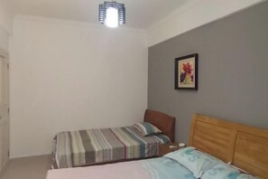 A bedroom with two single beds, a wooden headboard, a wall-mounted artwork, and a ceiling light fixture. - Loushanglou Seascape Motel (Sanya)