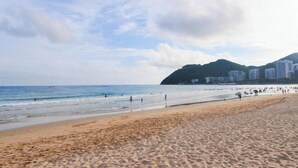 Una playa con gente, cielo despejado y edificios al fondo.