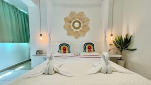 Una cama con toallas, un adorno en la pared con forma de flor y una planta en la mesita de noche.