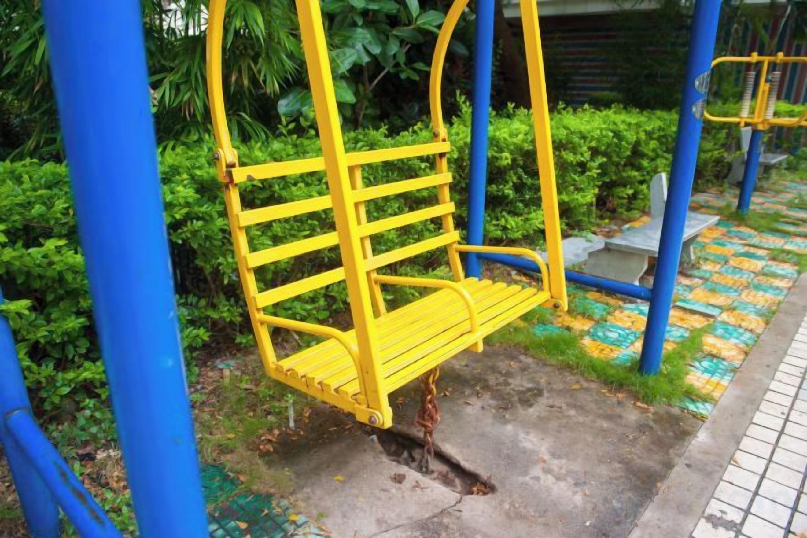 A yellow swing set with a chain and blue support structure in a park.