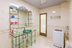 A bathroom with a glass sink, a mirror, shelves with toiletries, and a radiator. - Loushanglou Seascape Motel (Sanya)