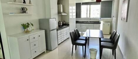 Una cocina moderna con armarios blancos, una mesa de comedor con cuatro sillas y una lámpara colgante roja.