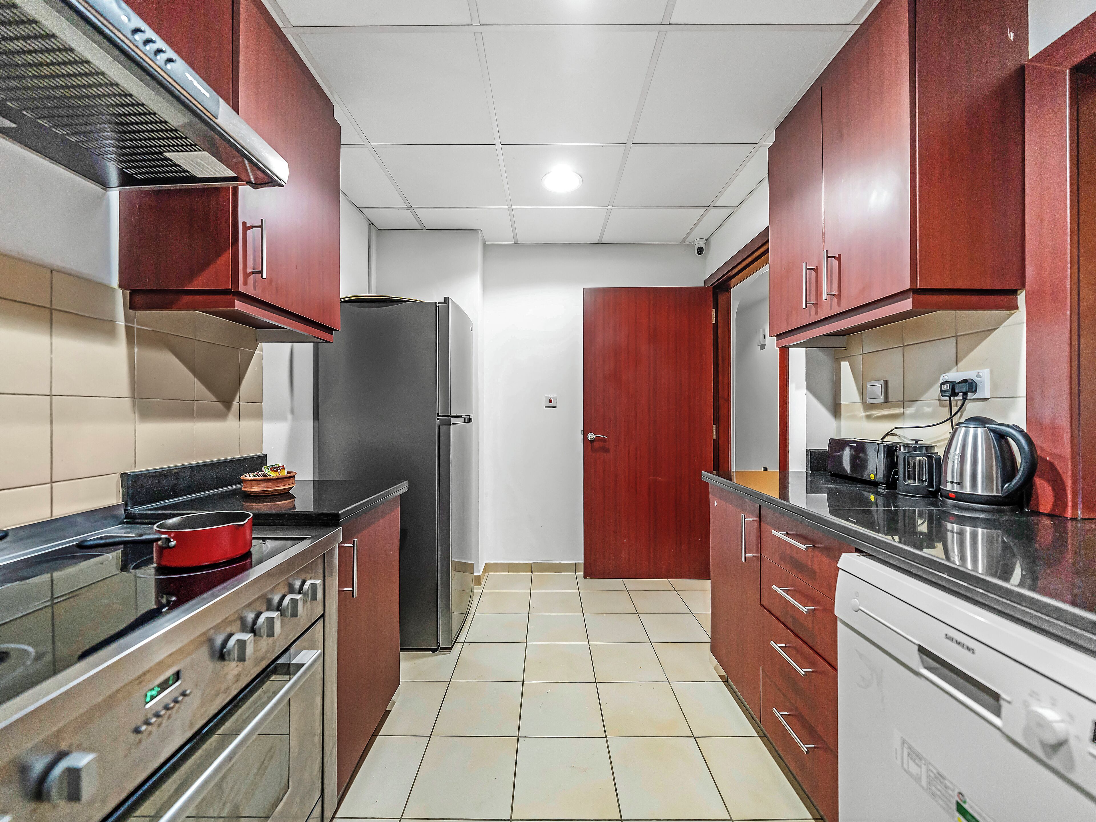 A kitchen with wooden cabinets, a stainless steel refrigerator, a stove, and a dishwasher.