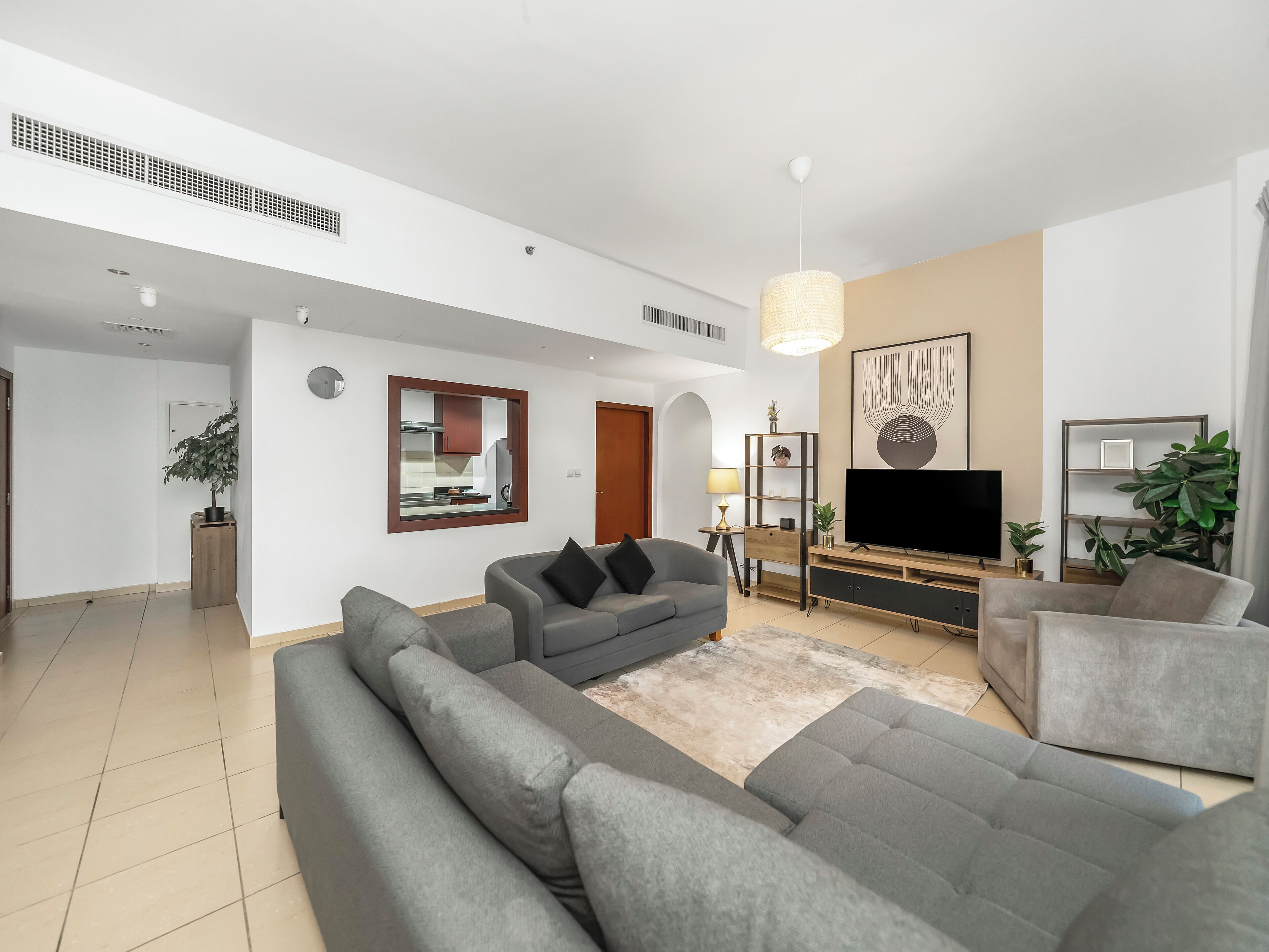 A modern living room with a grey sectional sofa, a flat-screen TV, a wooden entertainment unit, and a large mirror.