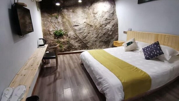 A bedroom with a bed, wooden headboard, a wall with a rock-like texture, a small plant, and a wooden bench. - Youran Inn (Yueqing)