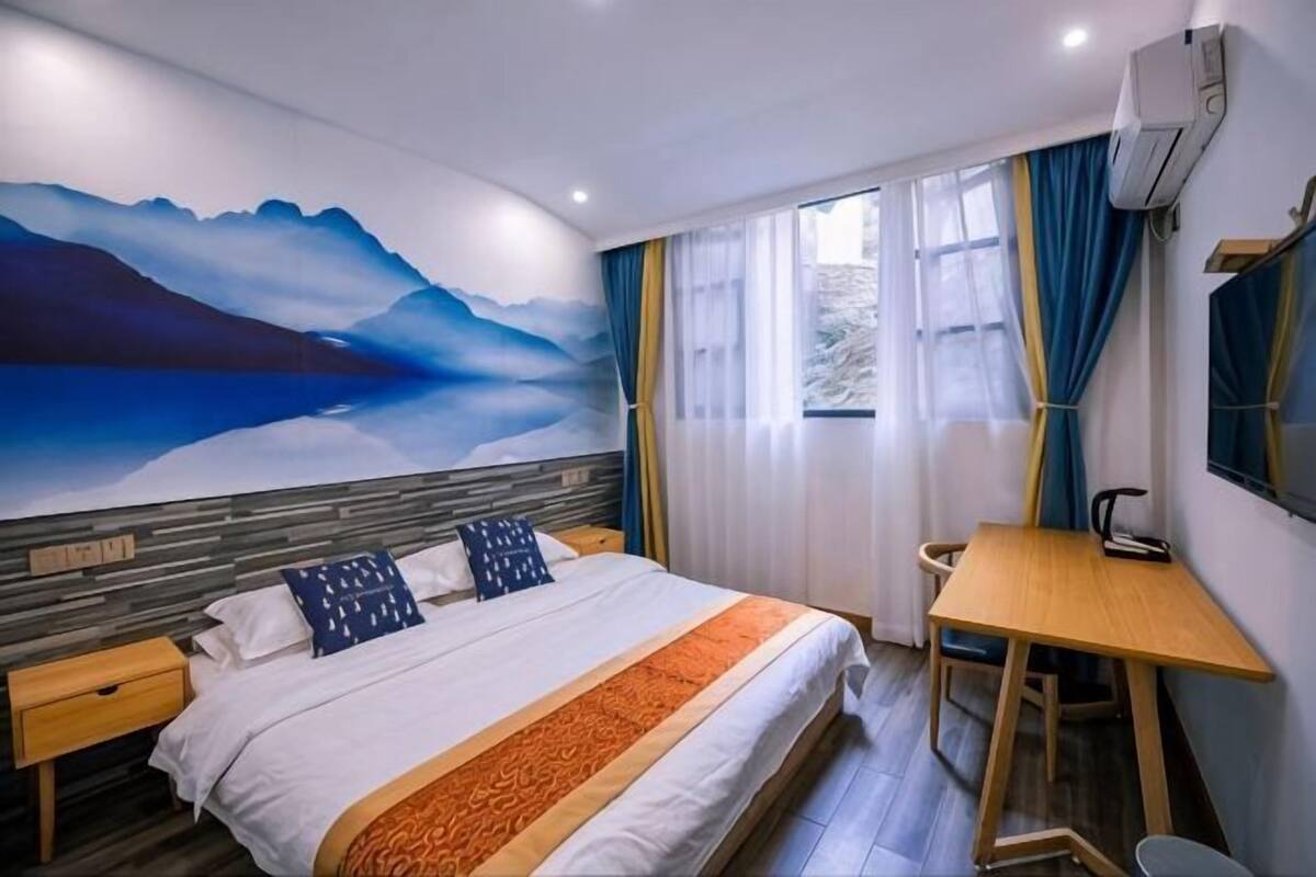 Een slaapkamer met een bed, een bureau, een stoel, een raam met gordijnen en een muurschildering.
