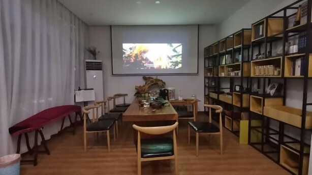 A modern dining area with a wooden table and chairs, a large bookshelf, and a projector screen displaying an image. - Youran Inn (Yueqing)