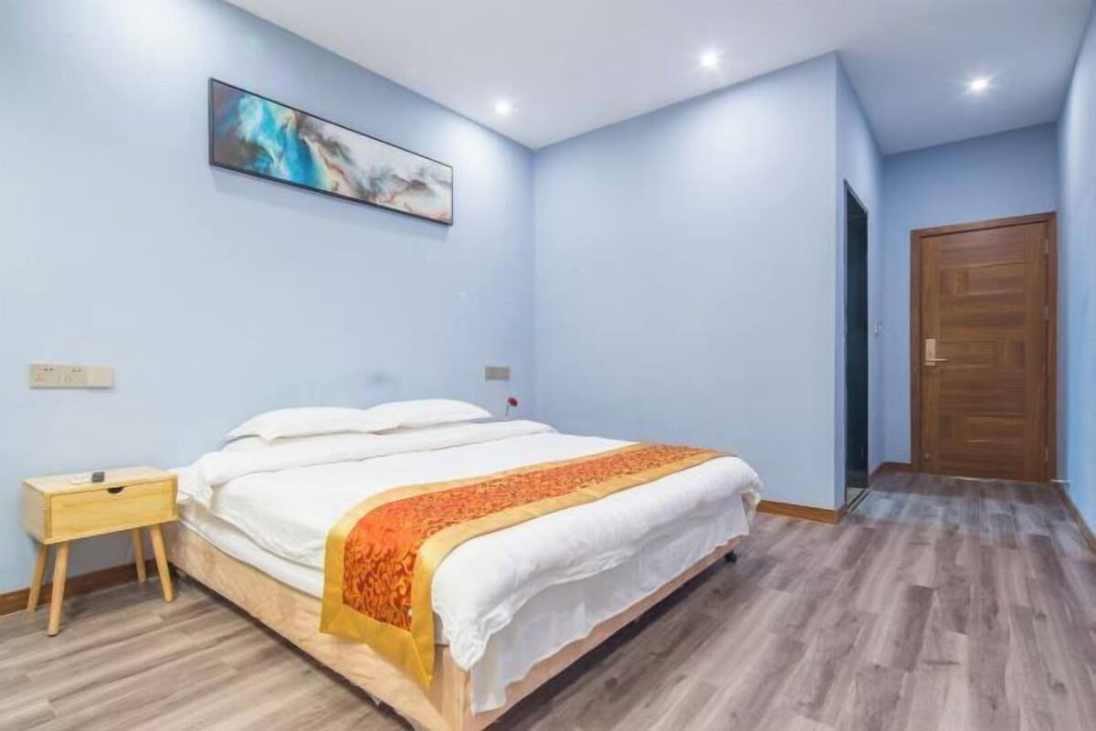 Een slaapkamer met een bed, een nachtkastje, een houten vloer, een deur en een schilderij aan de muur.