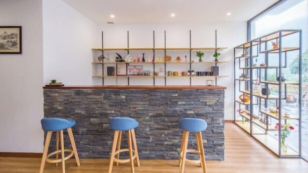 A modern kitchen with a stone countertop, three bar stools, and a large window with a view of greenery. - Youran Inn (Yueqing)