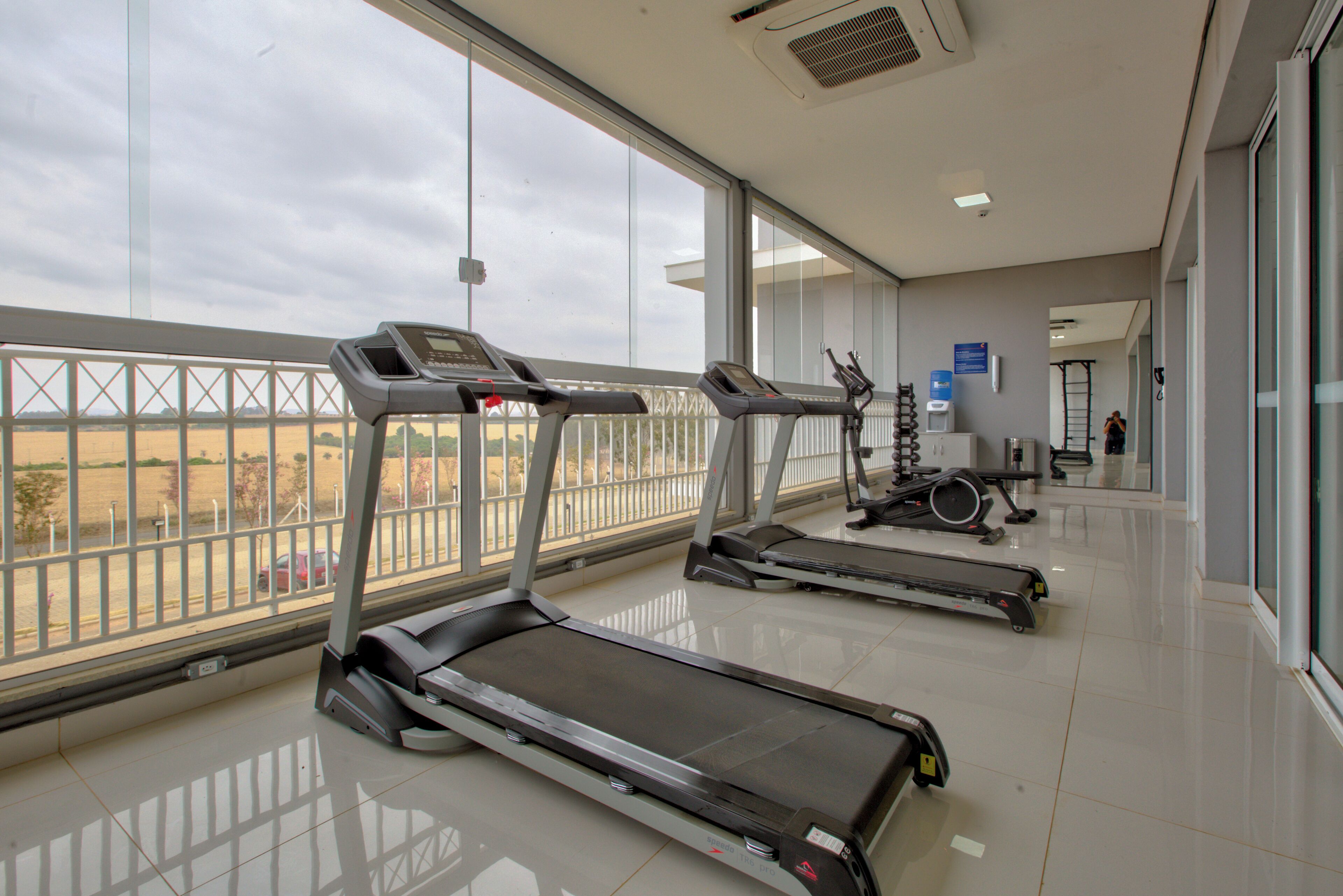 Una palestra con tapis roulant e attrezzature per esercizi, ampie finestre e un design moderno e pulito.